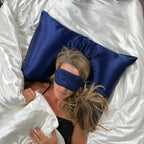 Person lying on a bed with a blue satin pillow and matching eye mask.