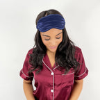 Woman wearing a maroon satin pajama set with white trim and a navy sleep mask.