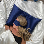 Person lying on a bed with a blue satin eye mask and pillow