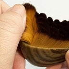 Hand holding a lymphatic brush with a wooden handle and brown bristles against a white background